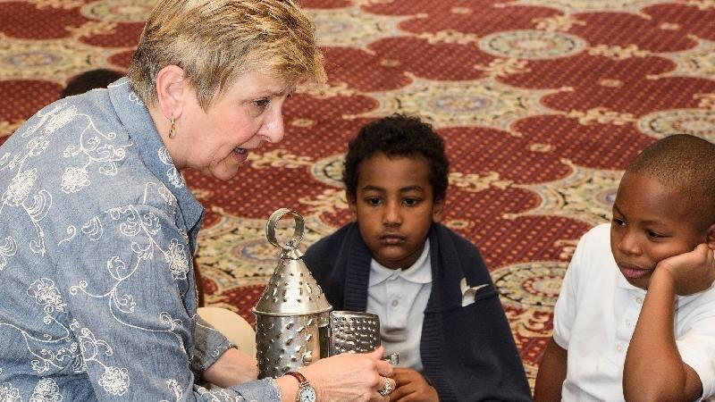 A volunteer shows students a tin lantern during a program.